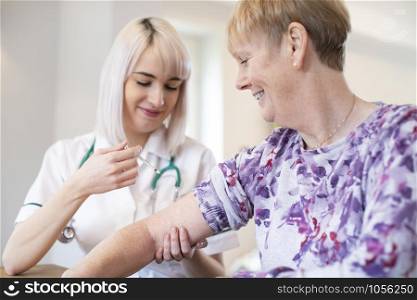 Female Nurse Giving Senior Woman Injection In Arm With Syringe