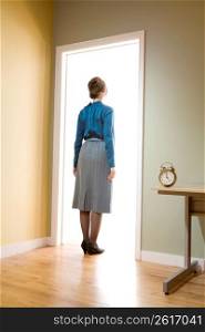 Female office worker standing in a doorway looking into a room illuminated with light