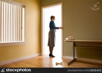Female office worker standing in an office doorway looking into a room illuminated with light, phone left off the hook