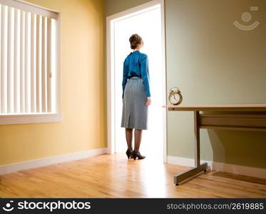 Female office worker standing in an office doorway looking into a room illuminated with light