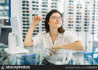 Female optician and consumer chooses glasses frame in optics store. Selection of spectacles with professional optometrist. Female optician and consumer chooses glasses frame