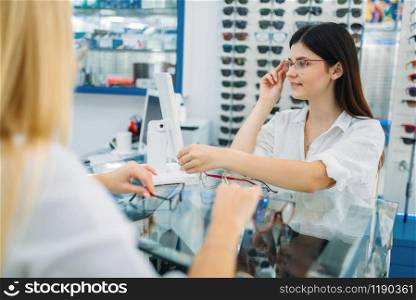Female optician and consumer chooses glasses frame in optics store. Selection of spectacles. Female optician and consumer chooses glasses frame