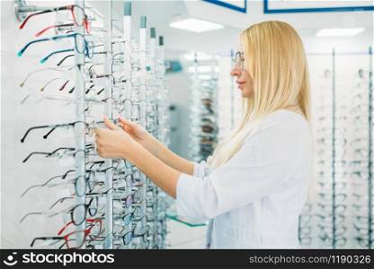 Female optometrist shows glasses in optics store. Selection of eyeglasses with professional optician, optometry. Female optometrist shows glasses in optics store