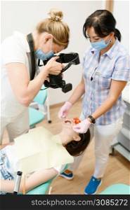 Female orthodontist, assistant and patient in clinic, stomatology. Doctor in uniform, medical worker, medicine and health, professional mouth care, dentistry, dentist makes teeth photo. Female orthodontist, assistant and patient, clinic