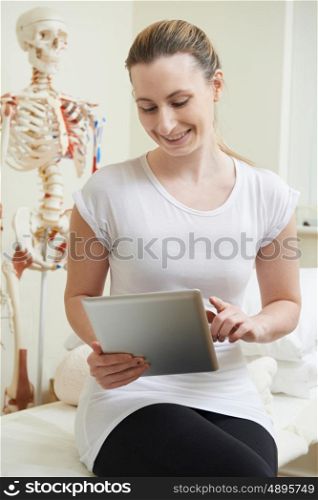 Female Osteopath In Consulting Room Using Digital Tablet