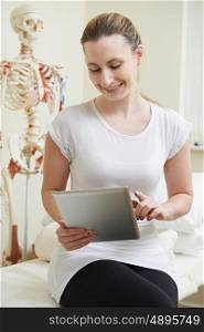 Female Osteopath In Consulting Room Using Digital Tablet