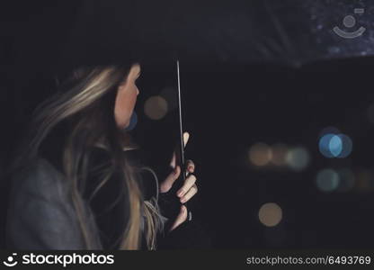 Female outdoors in rainy night, elegant woman under black umbrella looking on the city lights, city life, loneliness and melancholy concept. Female outdoors in rainy night