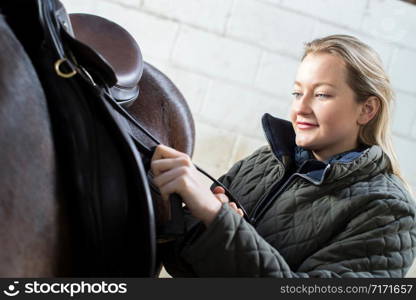 Female Owner Adjusting Saddle Straps In Stable With Horse