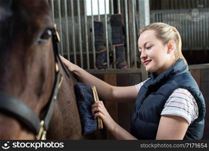 Female Owner In Stable Grooming Horse With Brush