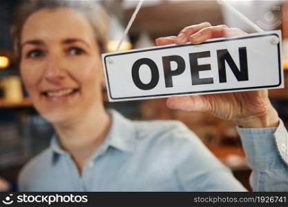 Female Owner Of Small Business Turning Round Open Sign On Door