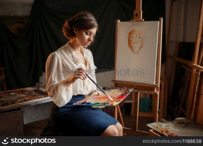 Female painter holds color palette and brush in studio. Creative paintbrush art, artist drawing in class, workshop interior on background. Female painter holds color palette and brush
