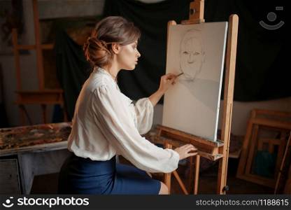 Female painter in studio, pencil sketch on easel. Creative paint, woman drawing portrait, workshop interior on background. Female painter in studio, pencil sketch on easel