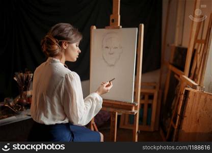 Female painter in studio, pencil sketch on easel. Creative paint, woman drawing portrait, workshop interior on background