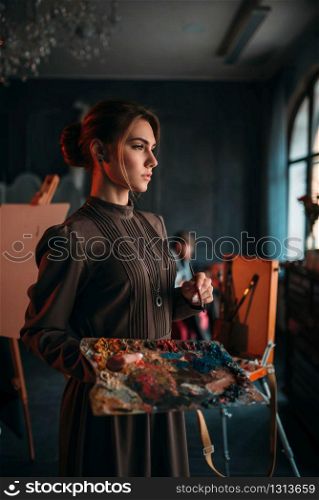 Female painter with brush and palette in hands in art studio. Oil paint, paintbrush drawing. Female painter with brush and palette in hands