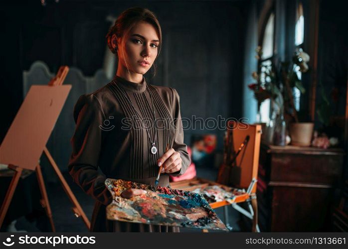 Female painter with brush and palette in hands in art studio. Oil paint, paintbrush drawing