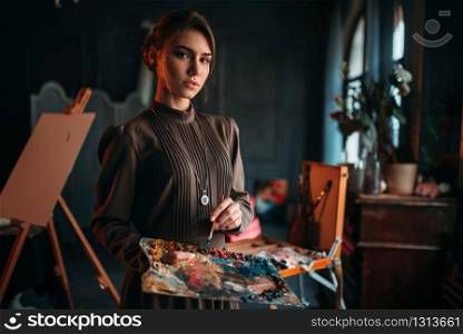 Female painter with brush and palette in hands in art studio. Oil paint, paintbrush drawing