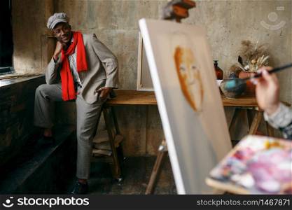 Female painter with brush draws male model in art studio. Artist at her workplace, creative master at the easel in workshop. Female painter with brush draws male model