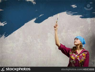 Female painter. Young woman in headscarf painting wall with brush