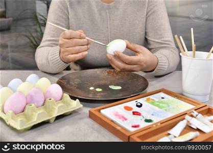 Female painting an egg surrounded by an assortment of painted eggs and a paint box on an out of focus background. Selective focus. Easter concept.