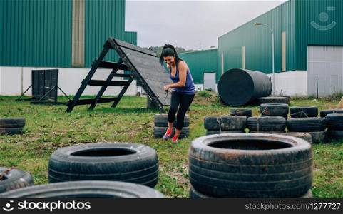 Female participant in an obstacle course dragging wheels seen from behind. Participant in an obstacle course dragging wheels