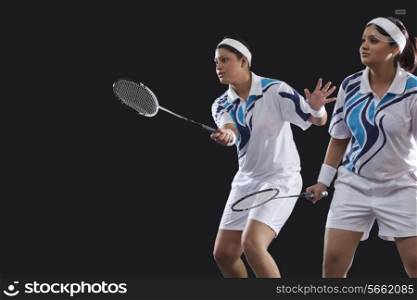 Female partners in sportswear playing badminton against black background