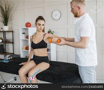 female patient physiotherapy with knee brace tape dumbbell