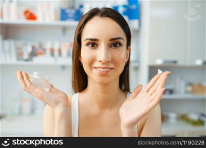 Female patient shows cream on finger in cosmetician office. Rejuvenation procedure in beautician salon. Cosmetic surgery against wrinkles, face and body care, skin therapy. Patient shows cream on finger, cosmetician office