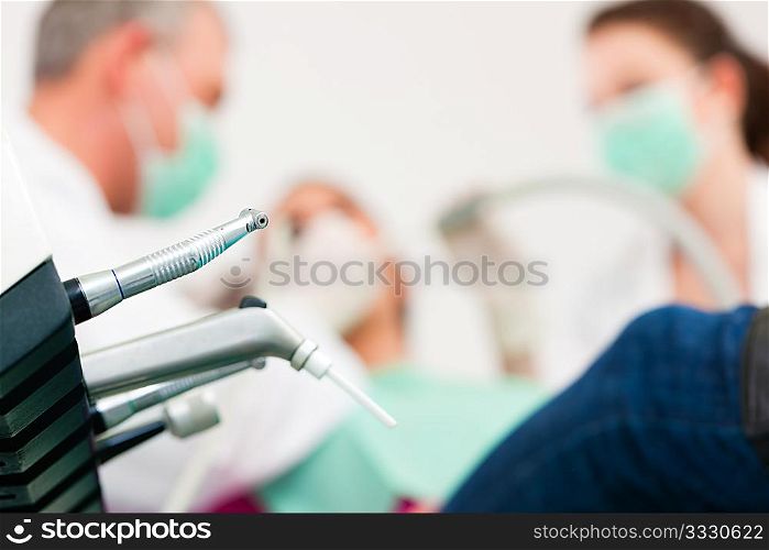 Female patient with dentist and assistant in a dental treatment, wearing masks and gloves, Dentist and assistant bowing over her using sucker and drill