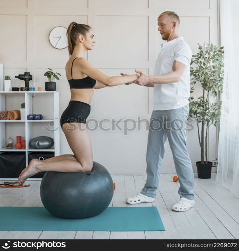 female patient with male physiotherapist doing exercises with ball