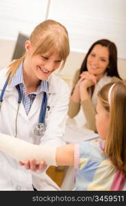 Female pediatrician checking bandage of girl broken arm