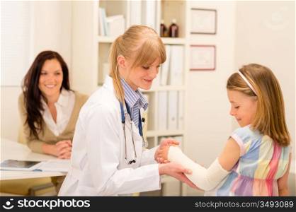 Female pediatrician checking bandage of girl broken arm