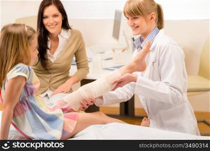 Female pediatrician checking broken bandaged leg of little girl