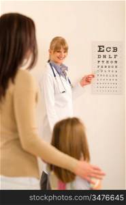 Female pediatrician ophthalmologist child pointing at eye chart medical office