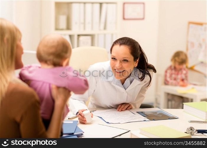 Female pediatrician smiling at baby patient sitting at office desk