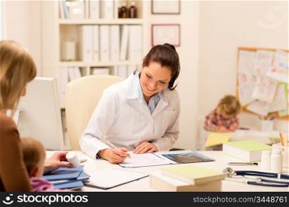 Female pediatrician smiling mother baby patient sitting at office desk