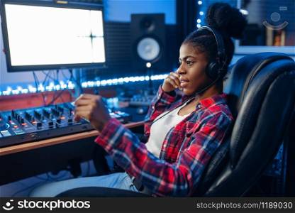 Female performer in headphones at the monitor in audio recording studio. Sound engineer at the mixer, professional music mixing