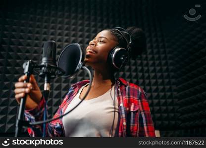 Female performer in headphones songs in audio recording studio. Musician listens composition, professional music mixing