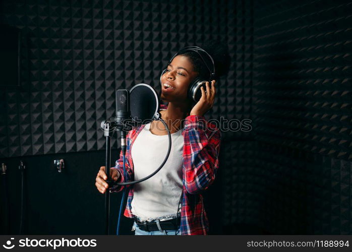 Female performer in headphones songs in audio recording studio. Musician listens composition, professional music mixing. Female performer songs in audio recording studio