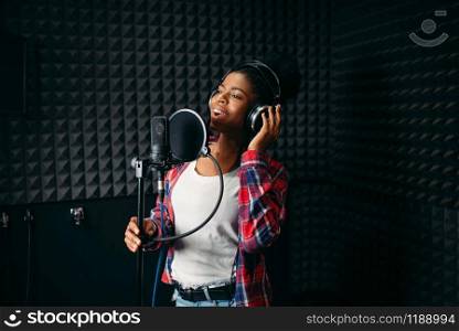 Female performer in headphones songs in audio recording studio. Musician listens composition, professional music mixing. Female performer songs in audio recording studio