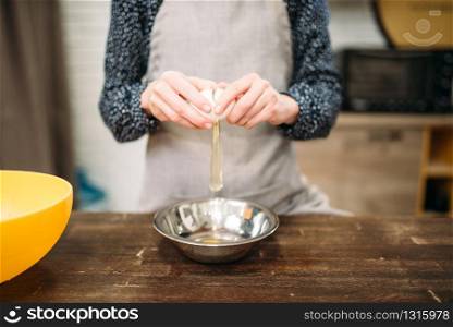 Female person breaks the egg into a bowl on wooden table. Sweet cake cooking preparation. Dough making