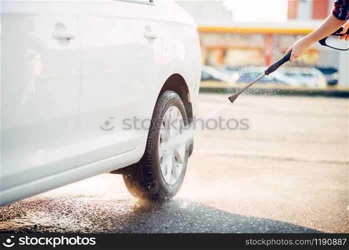 Female person cleans car wheels with high pressure water gun. Young woman on self-service automobile wash. Outdoor vehicle washing at summer day