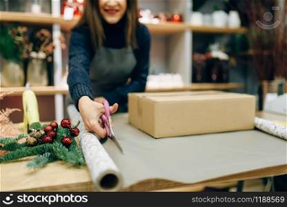 Female person cuts wrapping paper with scissors, gift box decoration. Woman wraps present on the table, handmade decor procedure