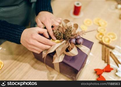 Female person decorates christmas gift box with fir cone, handmade wrapping and decoration process. Woman wraps present on the table, decor procedure