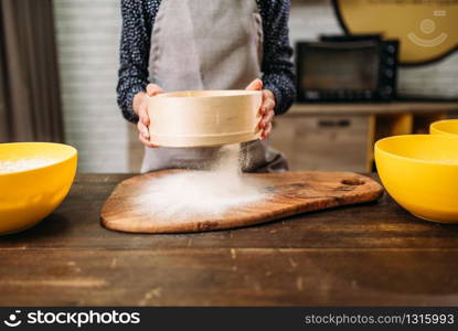 Female person filters the flour through a sieve on wooden table. Cake cooking. Dough preparation