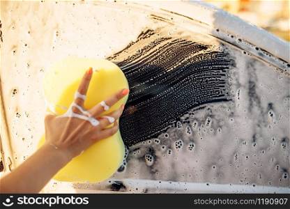 Female person hand with sponge scrubbing vehicle with foam, car wash. Young woman on self-service automobile washing. Outdoor carwash at summer day
