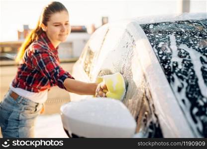 Female person hand with sponge scrubbing vehicle with foam, car wash. Young woman on self-service automobile washing. Outdoor carwash. Female person scrubbing vehicle with foam