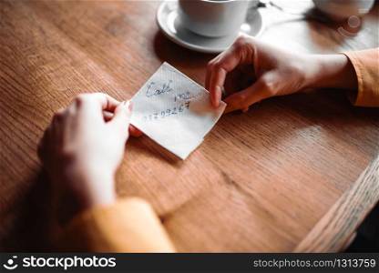 Female person hands holds love note with a phone number closeup view. Attractive proposal