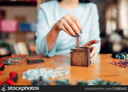 Female person hands pulls out a metal chain from a wooden box, master at work. Handmade jewelry. Needlework, bijouterie making