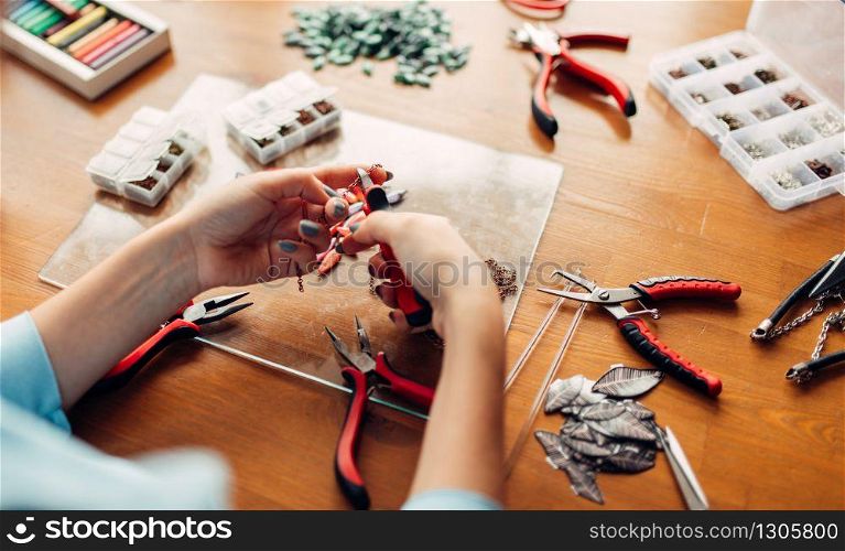 Female person holds pliers, master at workplace. Handmade jewelry. Needlework, fashion bijouterie making. Female person holds pliers, bijouterie making