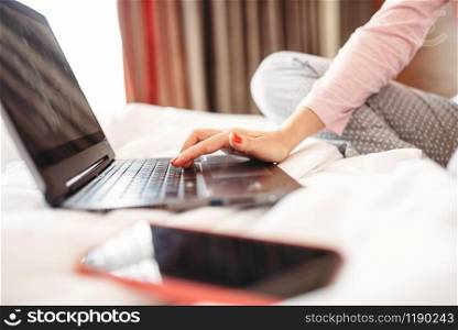 Female person in pajama drinks coffee and uses laptop in bed, good morning, bedroom interoir on background. Female person drinks coffee and uses laptop in bed